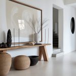 Minimalist foyer with a wooden console table, large abstract-framed artwork, and woven vases/baskets along a pale floor.