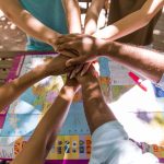 Group of people stacking hands over a world map, symbolizing teamwork outdoors.