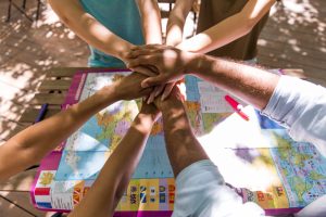 Group of people stacking hands over a world map, symbolizing teamwork outdoors.