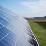Row of solar panels angled in a grassy field under a clear blue sky.