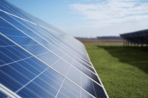 Row of solar panels angled in a grassy field under a clear blue sky.