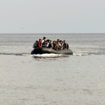 Crowded inflatable boat with many people wearing life jackets at sea the open ocean ahead.