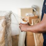 Person sealing a cardboard box with clear plastic wrap in a moving/packing scene