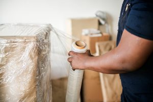 Person sealing a cardboard box with clear plastic wrap in a moving/packing scene