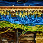 Close-up of a network patch panel with blue and yellow Ethernet cables neatly plugged into connectors, cables bundled in a data rack.