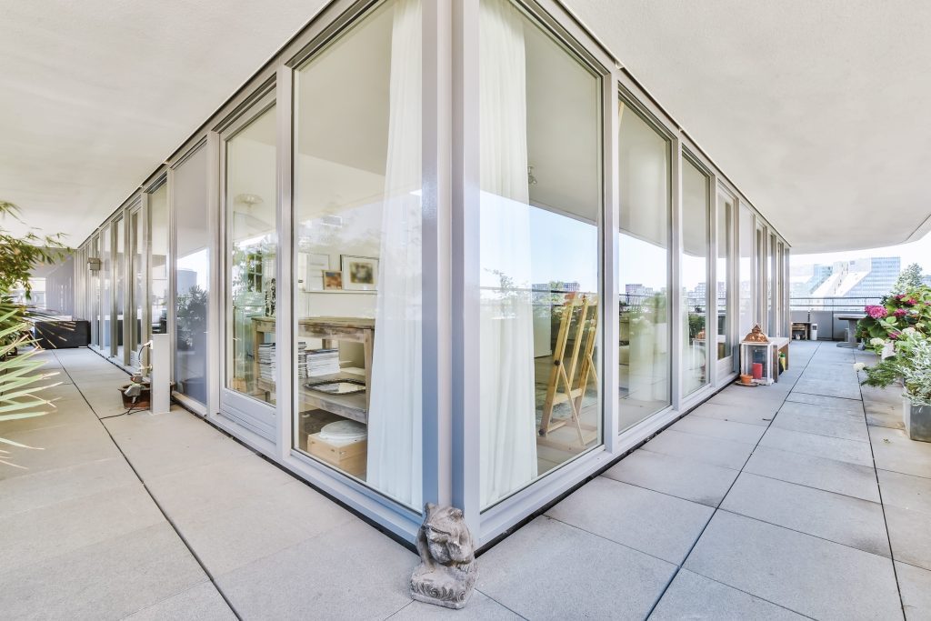 Contemporary glass-walled living space on a sunlit terrace with potted plants outside