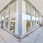 Contemporary glass-walled living space on a sunlit terrace with potted plants outside