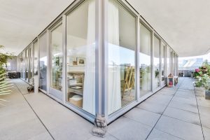 Contemporary glass-walled living space on a sunlit terrace with potted plants outside